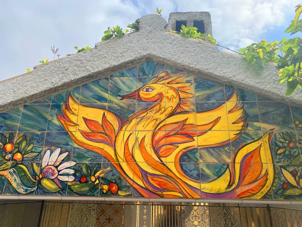 Detalle del frontón: ave de fuego dorada pintada a mano sobre azulejo cerámico
